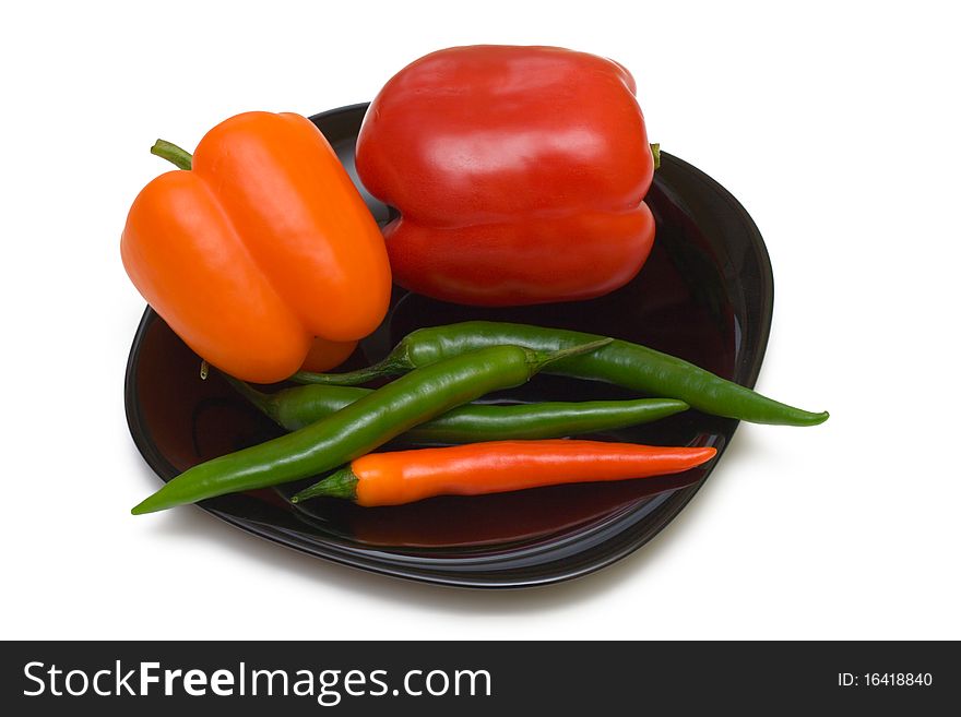 Bell and chilli peppers on black plate, isolated on white background