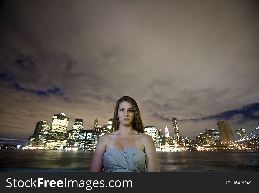 A young woman looks at you in front of a river and an urban skyline. A young woman looks at you in front of a river and an urban skyline