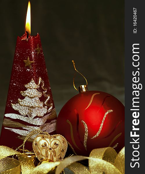 Christmas still life - red burning candle with evening ball and little gold heart on dark green background. Christmas still life - red burning candle with evening ball and little gold heart on dark green background