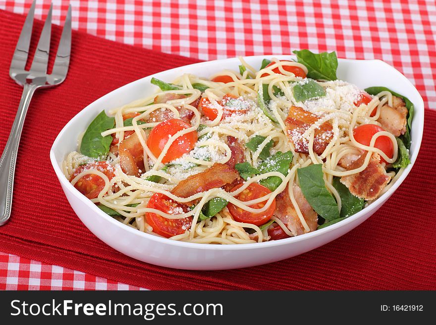 Spaghetti with bacon, tomatoes, and baby spinach in a serving bowl. Spaghetti with bacon, tomatoes, and baby spinach in a serving bowl
