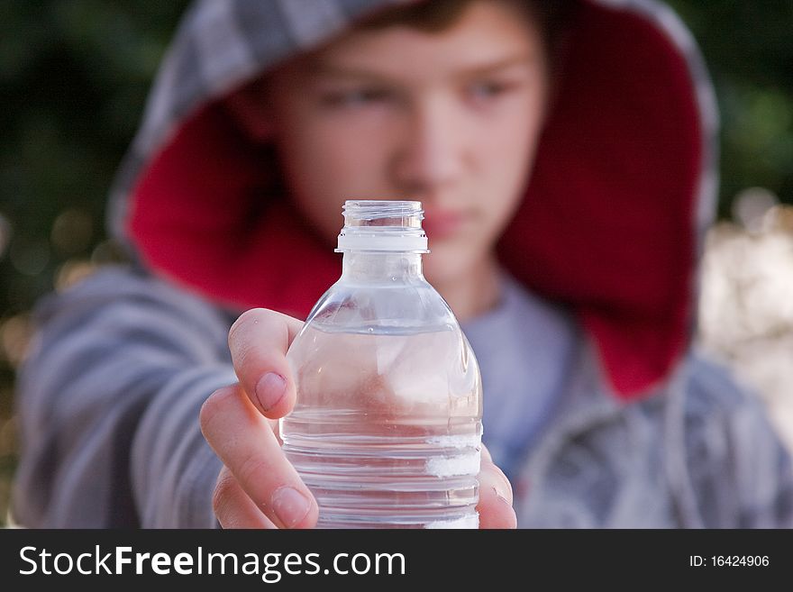 A young man holding out a bottle of cool, water.