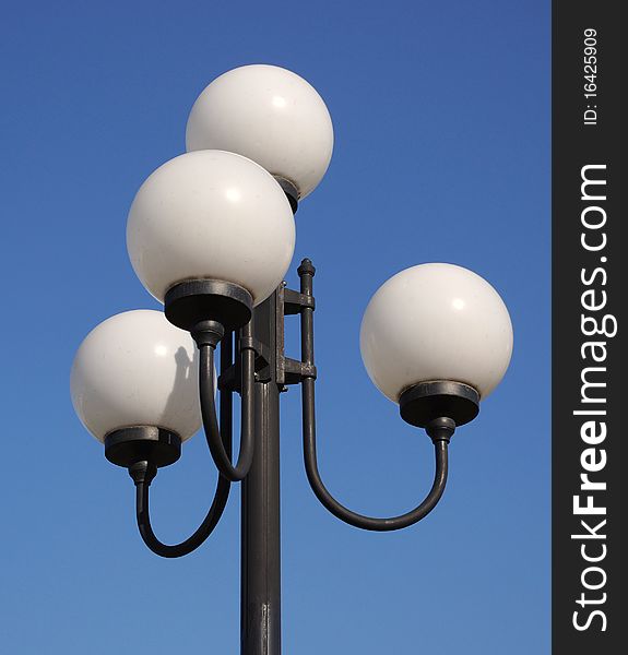 Street  lamp in form of white balls in sunny day on a blue sky background