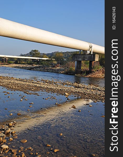 Transition of two pipelines of a high pressure through mountain small river in a summer landscape. Transition of two pipelines of a high pressure through mountain small river in a summer landscape