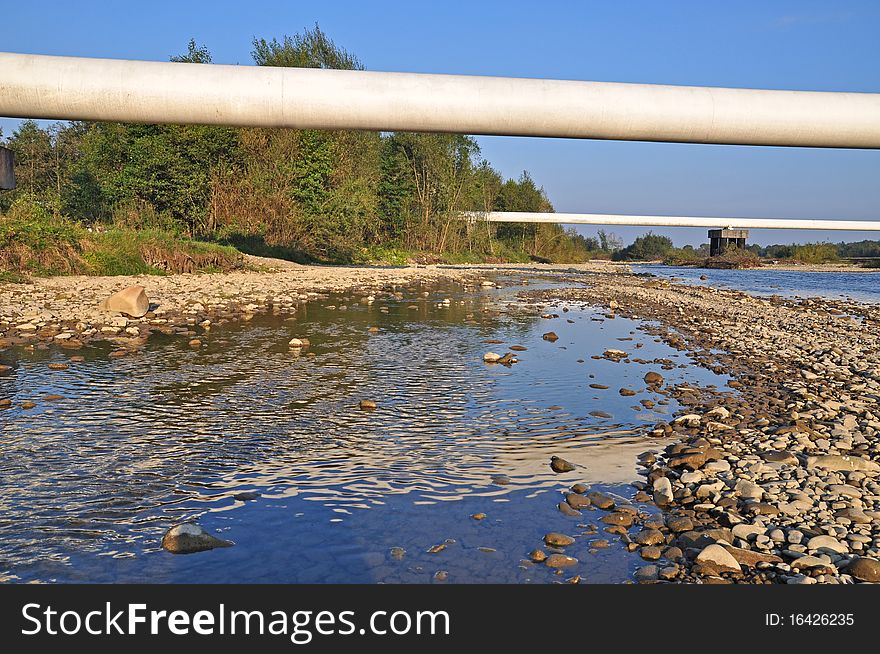 Transition of two pipelines of a high pressure through mountain small river in a summer landscape. Transition of two pipelines of a high pressure through mountain small river in a summer landscape