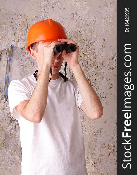 Builder looking through binoculars at the background of the plastered walls