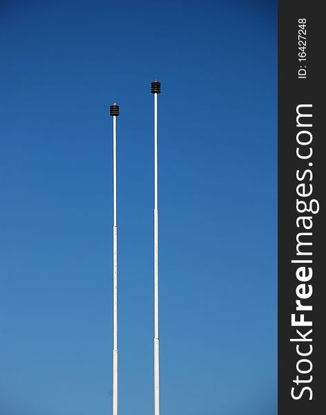 Two isolated flagpoles with clear blue sky in background to put your own flag on. Two isolated flagpoles with clear blue sky in background to put your own flag on