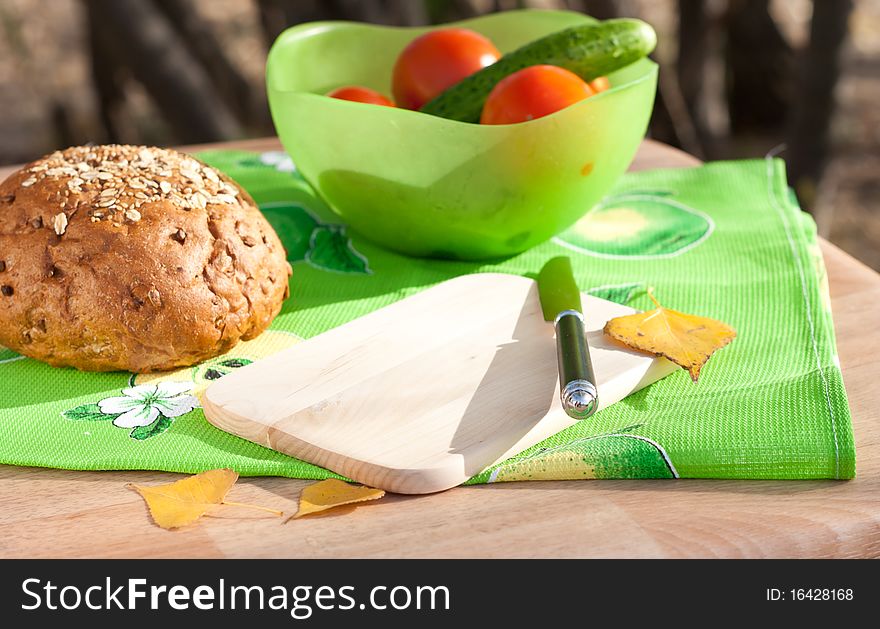 Bread and vegetables near the empty cutting board with yellow autumn leaves. Bread and vegetables near the empty cutting board with yellow autumn leaves