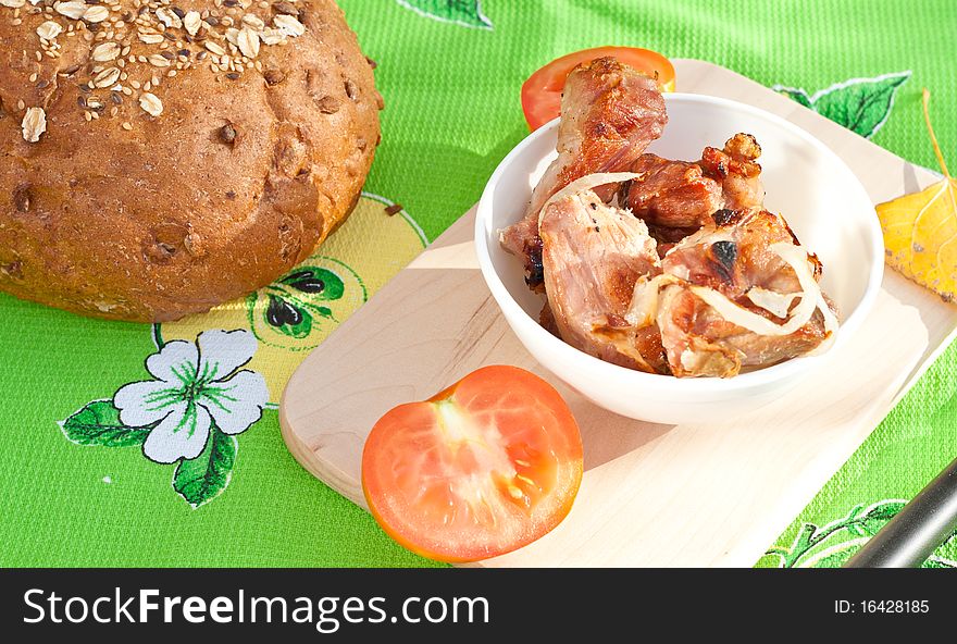 Grilled meat, tomatoes on the cutting board with loaf of rye bread. Grilled meat, tomatoes on the cutting board with loaf of rye bread