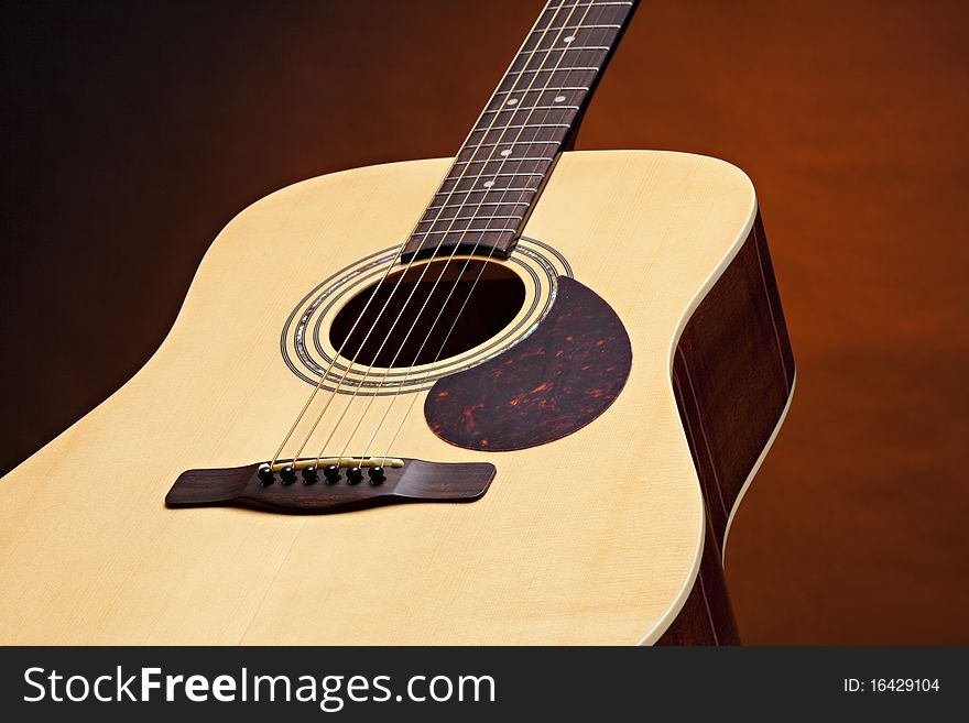 An acoustic guitar with a natural wood finish isolated on a spotlight gold background. An acoustic guitar with a natural wood finish isolated on a spotlight gold background.