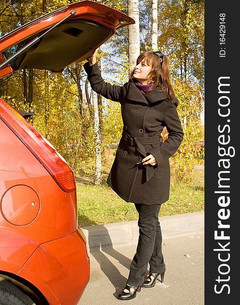 The girl closes a luggage place of the red car