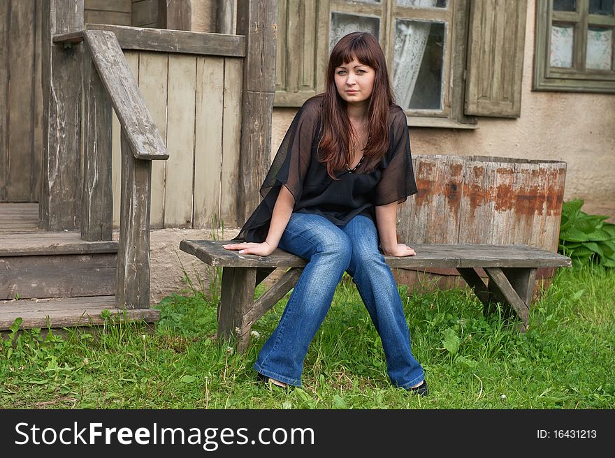 Young beautiful woman sit on the bench in front of old house. Young beautiful woman sit on the bench in front of old house.