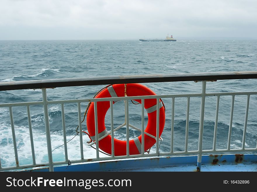 Red life-buoy on the ship's handrails with stormy sea backward; focus on handrails and buoy. Red life-buoy on the ship's handrails with stormy sea backward; focus on handrails and buoy