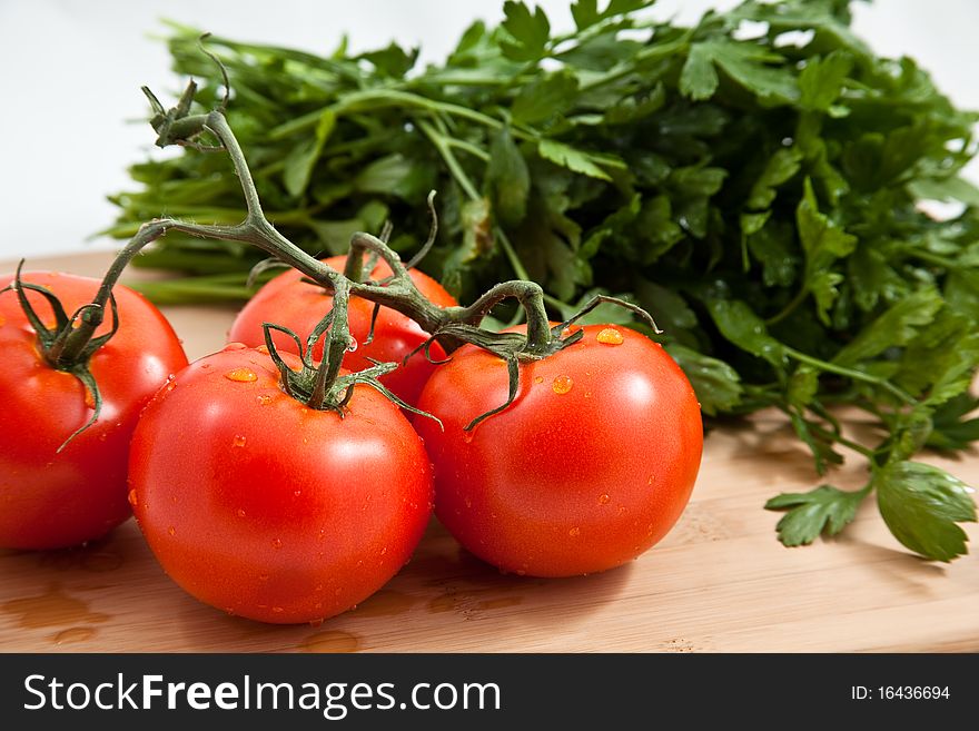 Fresh tomatos tomatoes on a bamboo cutting board with italian parsely in the background. Fresh tomatos tomatoes on a bamboo cutting board with italian parsely in the background