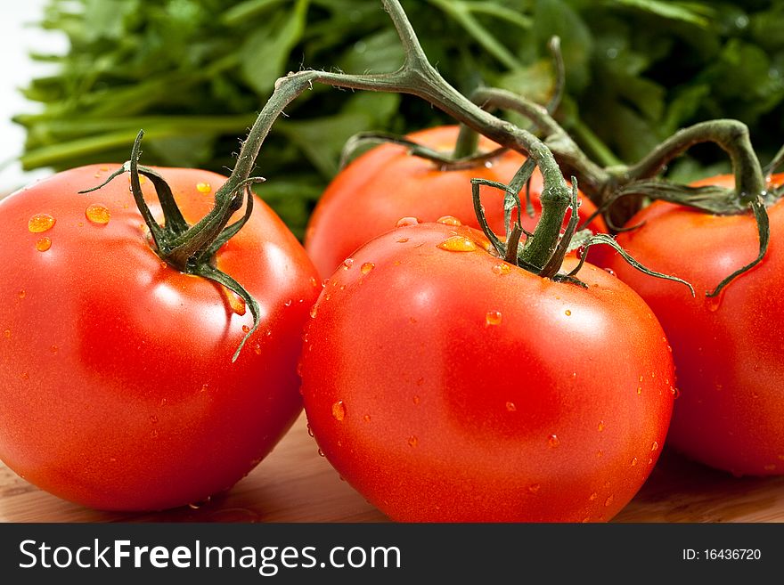 Fresh tomatos tomatoes on a bamboo cutting board with italian parsely in the background. Fresh tomatos tomatoes on a bamboo cutting board with italian parsely in the background