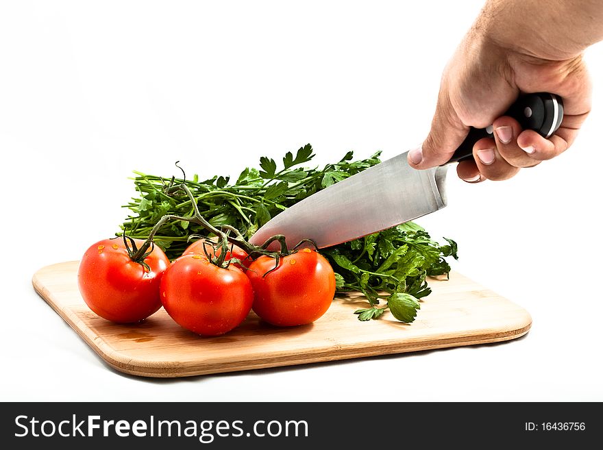 Fresh tomatos tomatoes on a bamboo cutting board with italian parsely in the background. Close crop isolated on white with a mans hand holding a chef knife. Fresh tomatos tomatoes on a bamboo cutting board with italian parsely in the background. Close crop isolated on white with a mans hand holding a chef knife