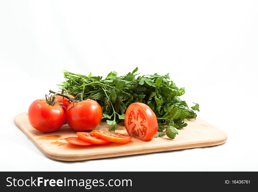 Fresh tomatos tomatoes sliced on a bamboo cutting board with italian parsely in the background. Close crop isolated on white. Fresh tomatos tomatoes sliced on a bamboo cutting board with italian parsely in the background. Close crop isolated on white