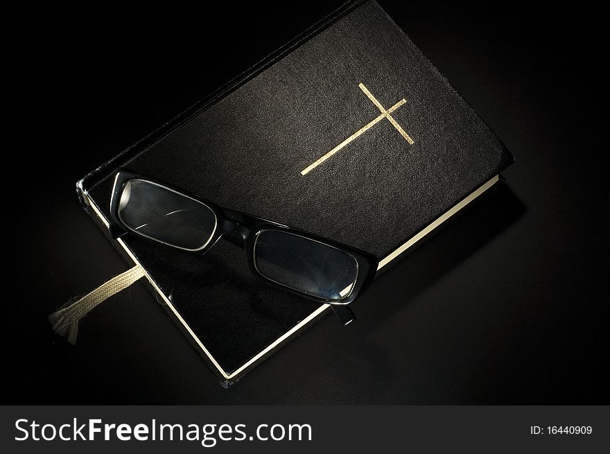 Bible with eyeglasses. Black background