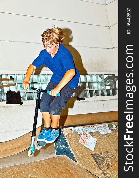 Boy goes airborne with his scooter in the skate hall