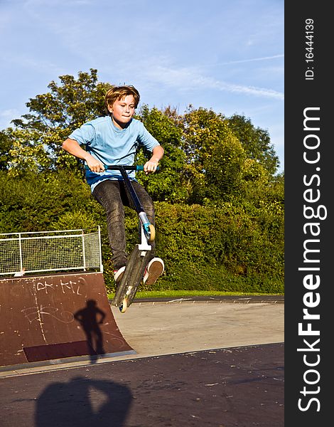 Boy jumps with scooter at the skate park over a ramp and has fun