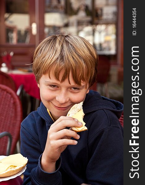 Portrait of a handsome smiling boy,sitting and eating a role outside