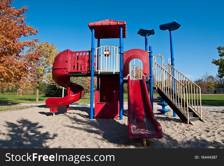 A neighborhood park with brightly colored playground equipment and trees in the fall. A neighborhood park with brightly colored playground equipment and trees in the fall.