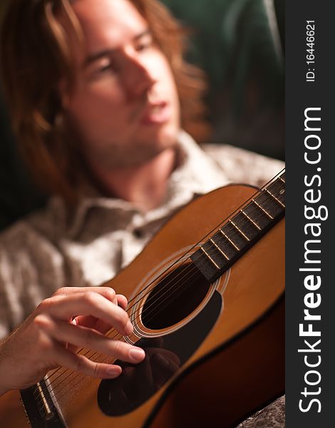 Young Musician Plays His Acoustic Guitar under Dramatic Lighting.