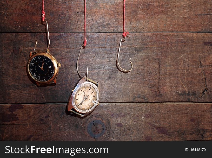 Two old watches hanging on fish hooks on wooden background. Two old watches hanging on fish hooks on wooden background