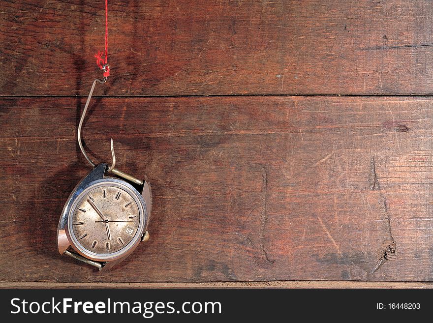 Old watch hanging on fish hook with red thread on wooden background. Old watch hanging on fish hook with red thread on wooden background