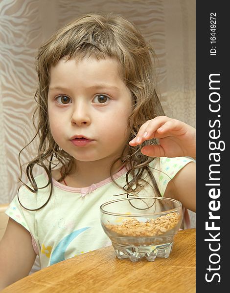 The thoughtful child sits at a table and wishes to take dry flakes from a dish