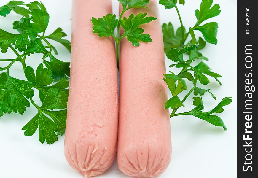 Two sausages on a white plate close up also are decorated by greens. Two sausages on a white plate close up also are decorated by greens