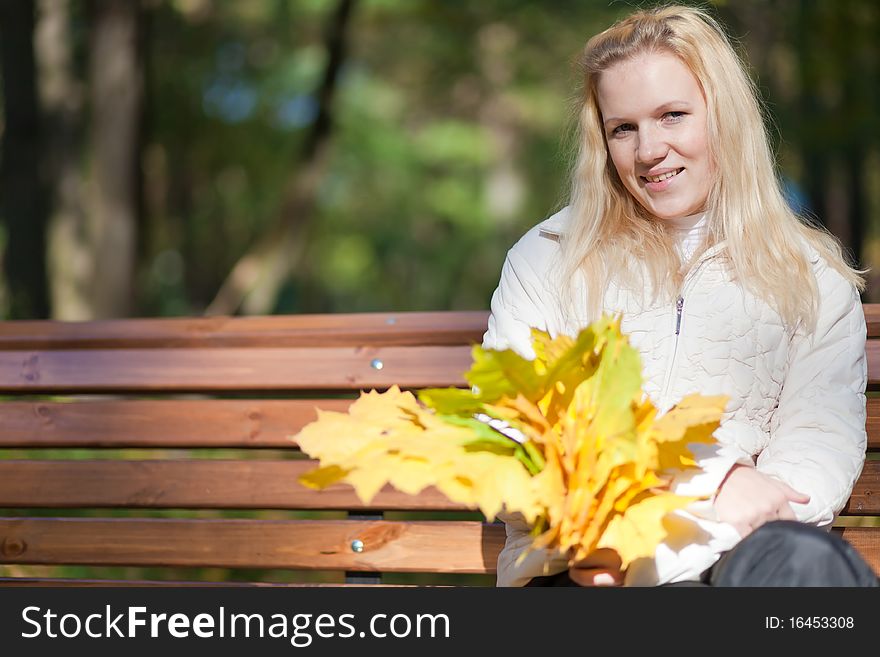 Girl sits on a bench and smiles autumn day