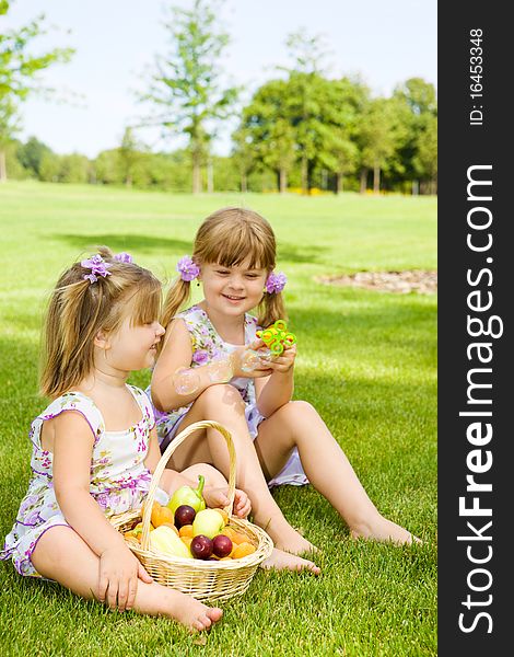 Two preschool sisters sitting in garden and playing with bubbles. Two preschool sisters sitting in garden and playing with bubbles