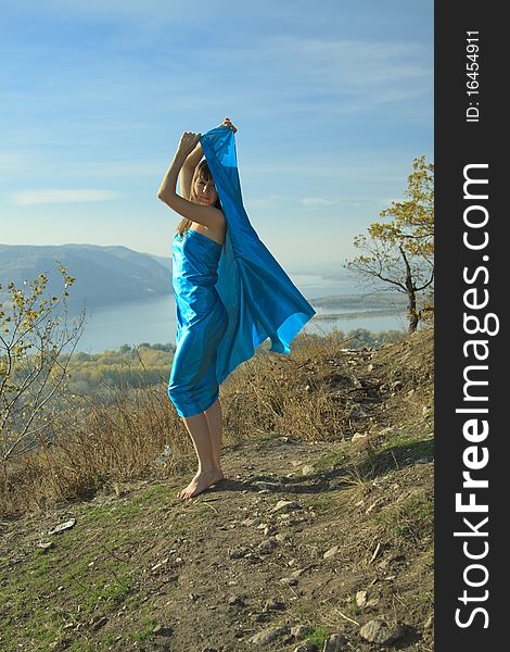 A young girl in a blue dress dancing on a mountain