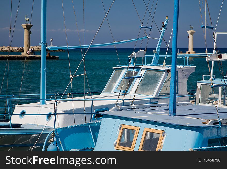 Typical Greek fishing boats are waiting in the harbor for departure. Two bronze deers guard the entrance to the Mandraki harbor. Typical Greek fishing boats are waiting in the harbor for departure. Two bronze deers guard the entrance to the Mandraki harbor.