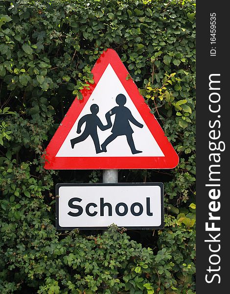 A triangular sign in a hedge warning of the presence of school children. A triangular sign in a hedge warning of the presence of school children