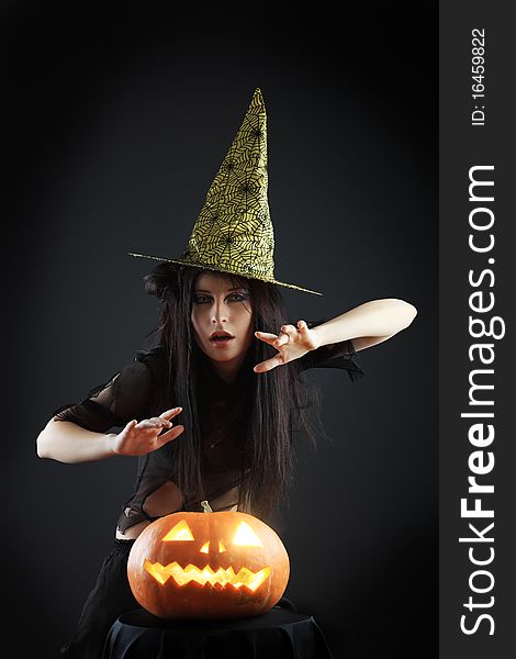 Halloween witch with a broom and carved pumpkin over black background.