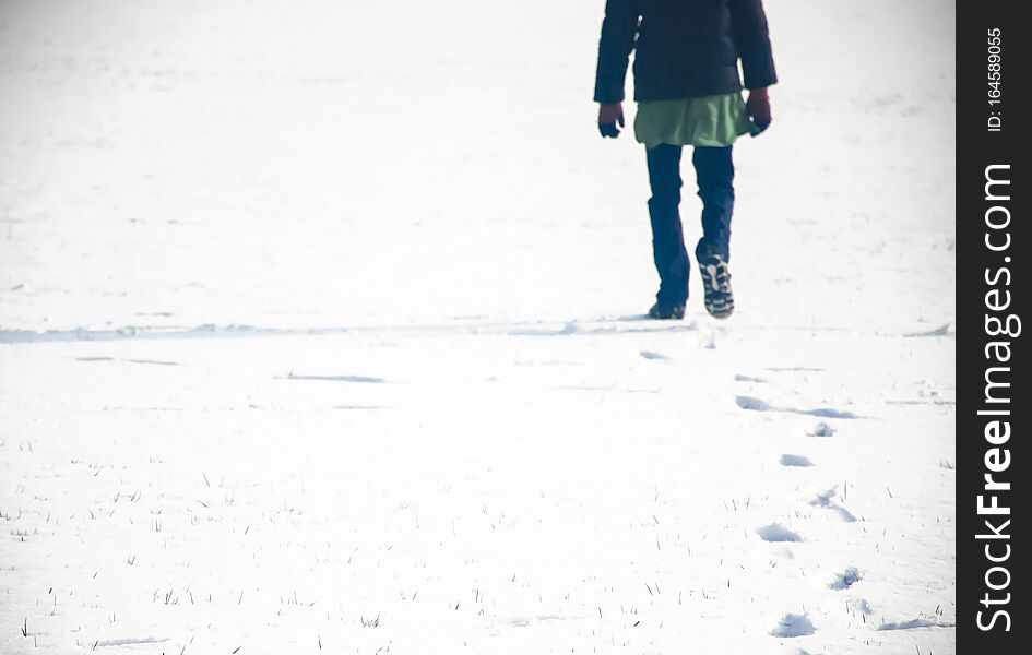 A person walking in fresh snow and making his foot marks in the snow. It is a boy in blue jeans and shoes.