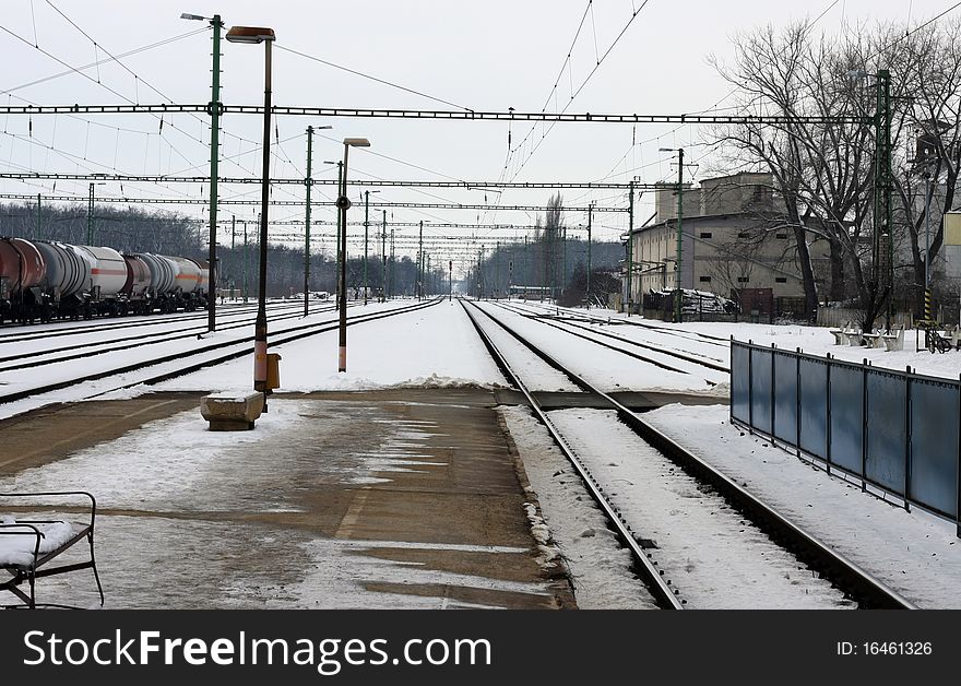 Railway station in winter. Snowy field between the rails and ice in the platform.