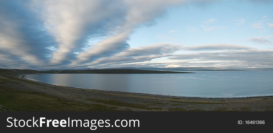 Wild lanscape of Finnmark see cost of Kafiord approaching Mageroya island, evening sun lights spectacular clods refrecting in water surfce