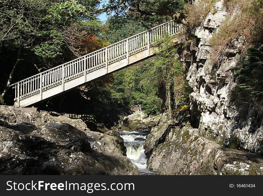 Wooden bridge, with railings, spanning a gorge with a river. Wooden bridge, with railings, spanning a gorge with a river.