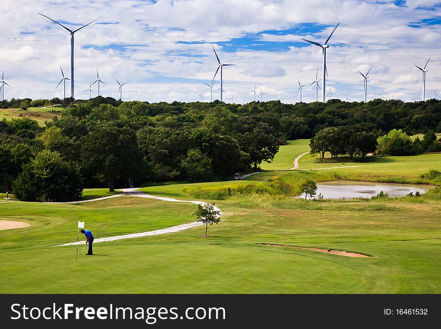 Wind generators on the horizon above a golf course with a golfer in the foreground. Wind generators on the horizon above a golf course with a golfer in the foreground