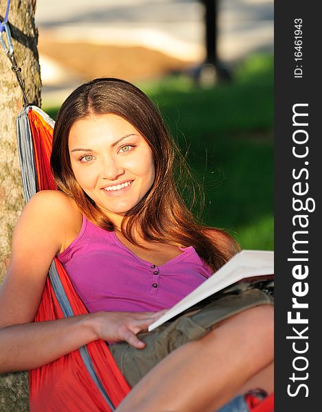 Happy young woman lying in a hammock and reading a book. Happy young woman lying in a hammock and reading a book