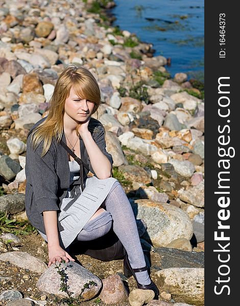 A teen girl sitting on a stone on a shore. A teen girl sitting on a stone on a shore.