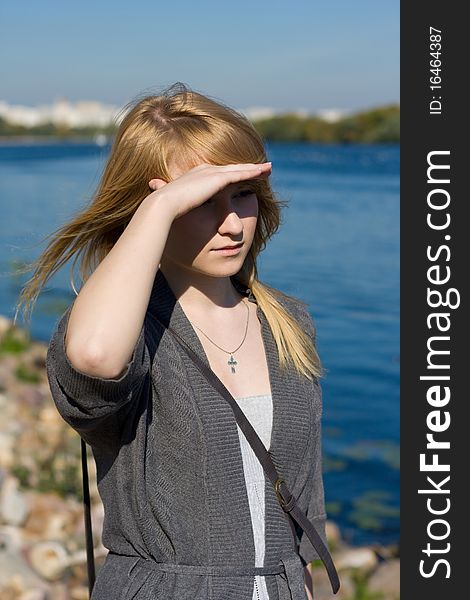 Caucasian teen girl with blond hair is standing on a shore and looking away. Caucasian teen girl with blond hair is standing on a shore and looking away.