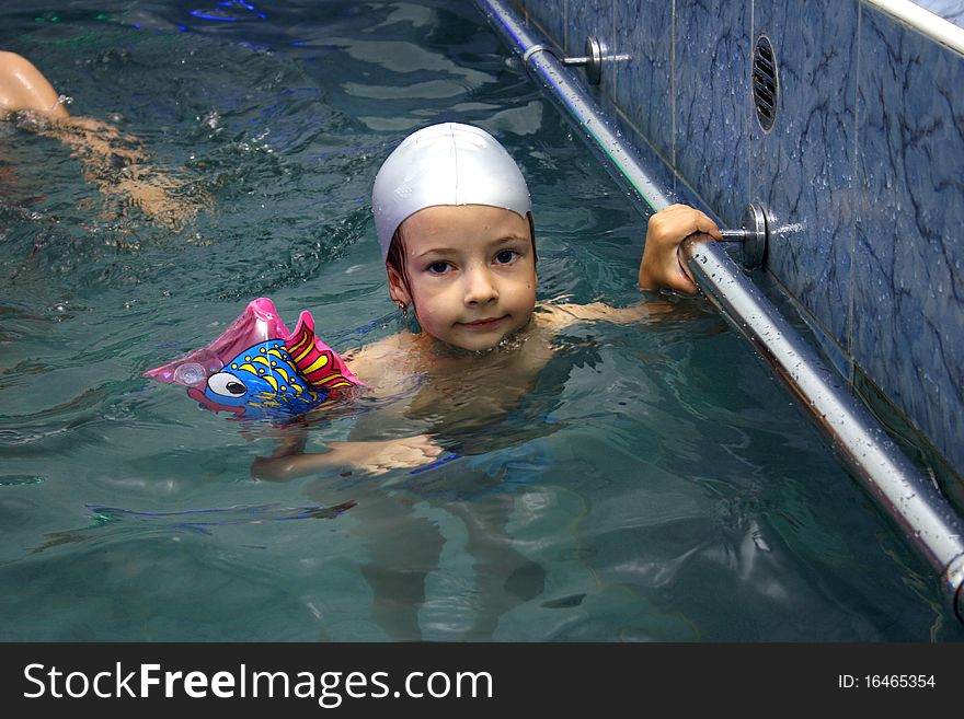 Girl in silver rubber swimming hat clinging to handrails in the pool. Girl in silver rubber swimming hat clinging to handrails in the pool