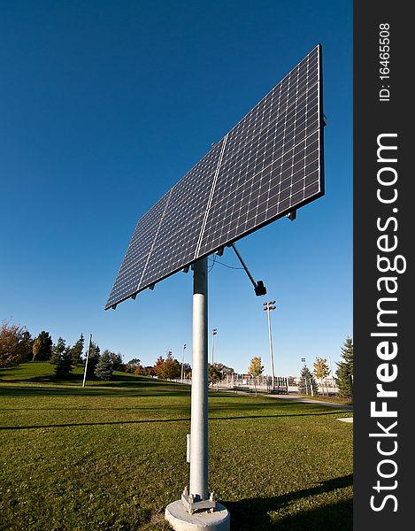 A photovoltaic solar panel array in a park with a blue sky in the background. A photovoltaic solar panel array in a park with a blue sky in the background.
