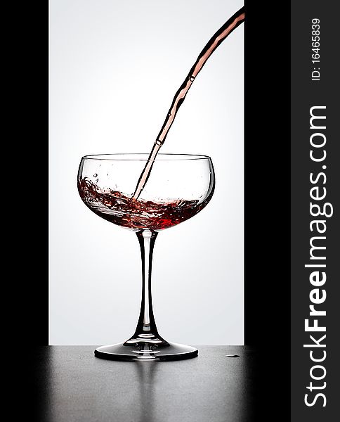 Dynamic action, red wine in glass bowl resting on a bench in front of a window. Dynamic action, red wine in glass bowl resting on a bench in front of a window