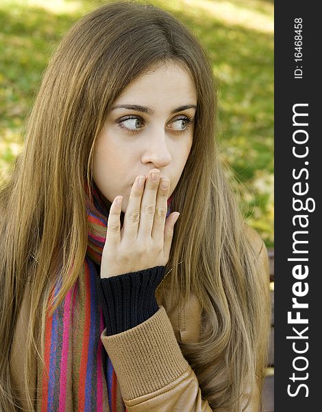 Vertical portrait of a beautiful young woman sitting on a bench in the park around a lot of yellow, red green leaves. Expressed surprise, shock. Vertical portrait of a beautiful young woman sitting on a bench in the park around a lot of yellow, red green leaves. Expressed surprise, shock