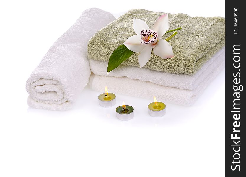 Stack of towels with white orchid flower and green burn scened candles isolated on white. Stack of towels with white orchid flower and green burn scened candles isolated on white