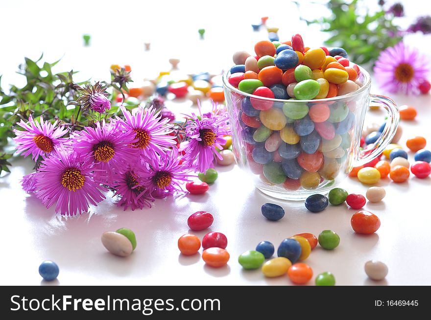 Varicoloured candies in a cup and pink flowers. Varicoloured candies in a cup and pink flowers